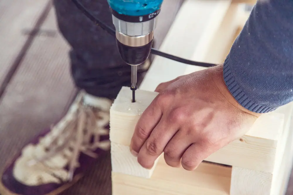 Drilling a pilot hole into a piece of timber held steady by hand